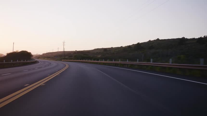 A point-of-view shot driving down a winding, empty highway through the countryside during a beautiful sunrise