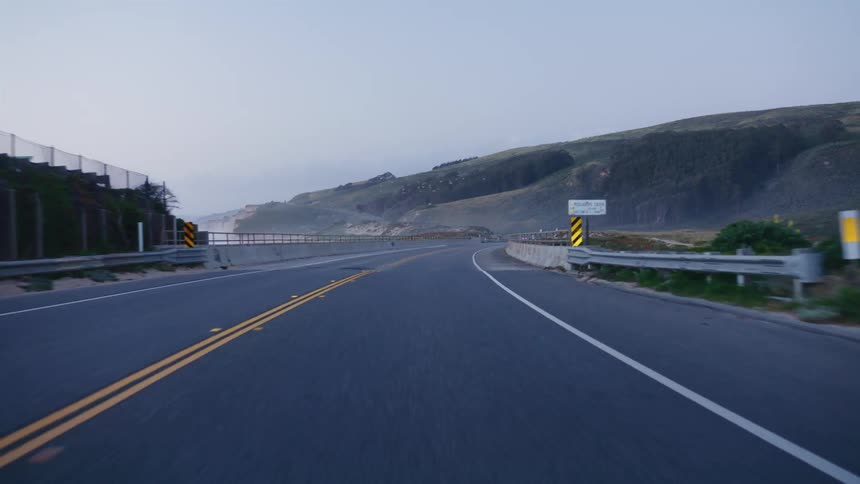 Point of view driving along a winding coastal highway in the early morning