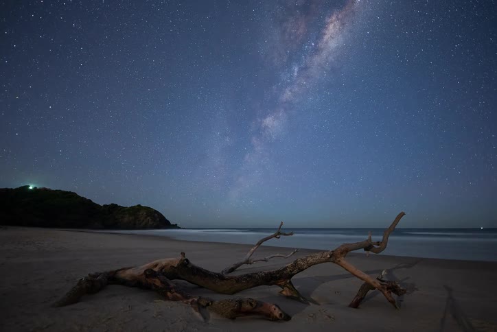 A stunning timelapse shows the Milky Way moving across the night sky above a deserted beach with driftwood in the foreground