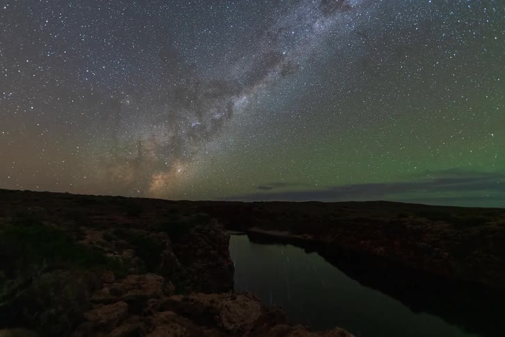 The Milky Way galaxy moves across the starry night sky with a faint green airglow in this stunning timelapse over a river canyon
