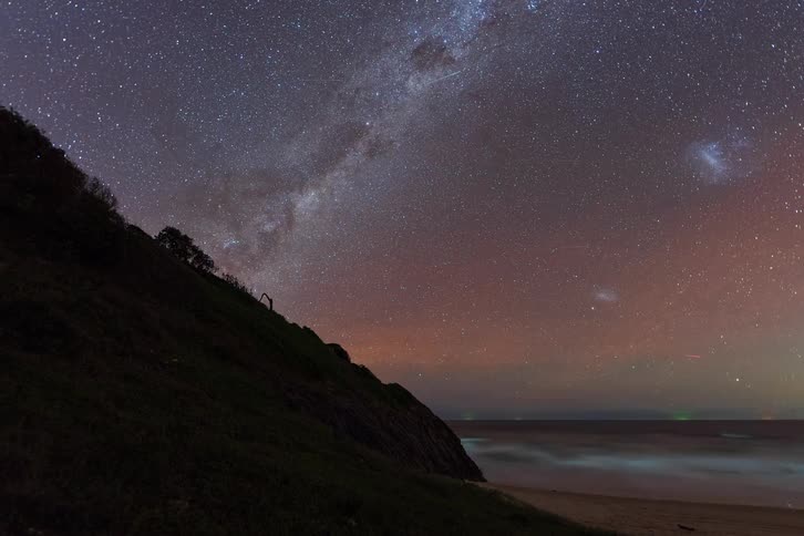 A stunning timelapse of the Milky Way galaxy and shooting stars moving across the night sky above a tranquil ocean beach
