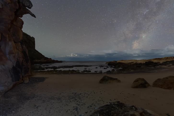 A stunning day-to-night timelapse shows the Milky Way rising over a secluded rocky beach cove as clouds drift by