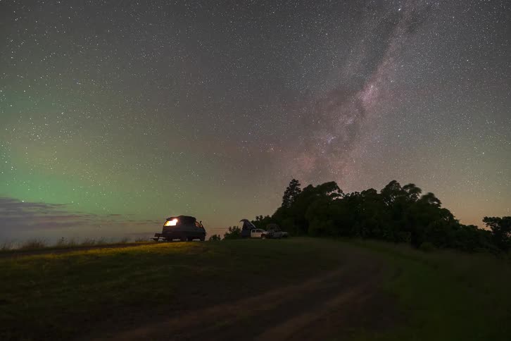 A breathtaking timelapse shows the Milky Way and green airglow moving across the night sky above a remote hilltop campsite