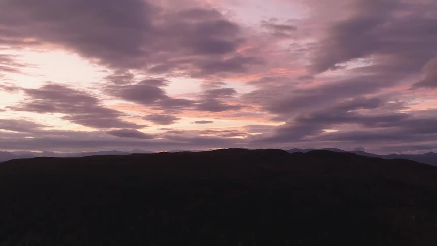 A dramatic purple and pink sky full of clouds hangs over a silhouetted mountain range at sunset