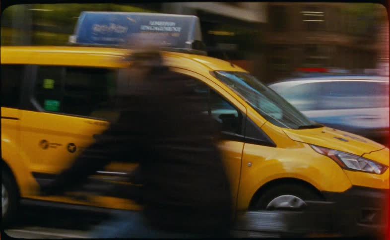 A yellow NYC taxi cab drives down a city street in this grainy, vintage-style footage