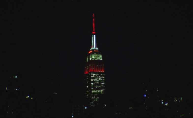 16mm film captures the Empire State Building illuminated in red and white against the night sky, featuring artistic light trail effects
