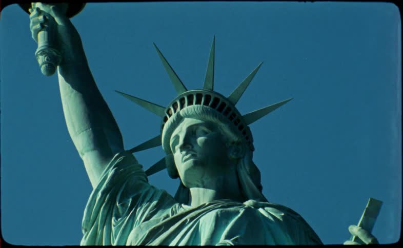 A vintage-style archival shot slowly pans up the iconic Statue of Liberty against a stark, cloudless blue sky