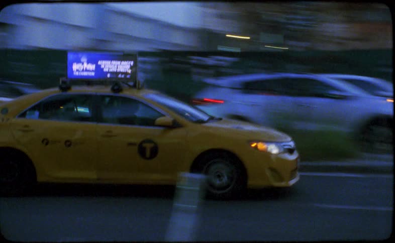 An iconic yellow taxi cab blurs through the streets of New York City at night in this grainy, vintage-style footage