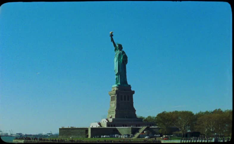 A vintage film captures a beautiful view of the Statue of Liberty against a clear blue sky from a boat in New York Harbor