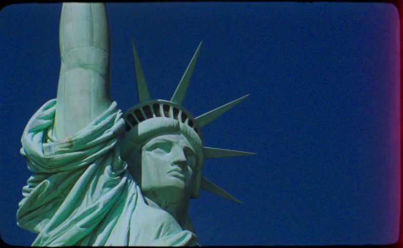 Vintage 16mm film captures a static close-up shot of the Statue of Liberty's face and crown against a solid blue sky