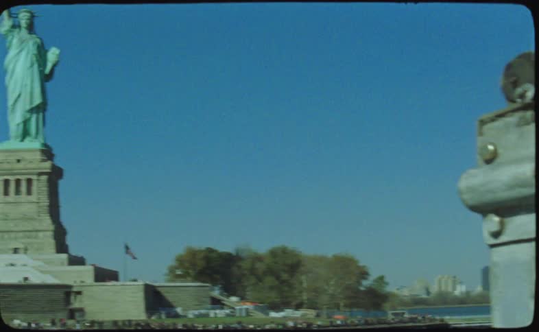 A vintage 16mm film captures the iconic Statue of Liberty standing tall against a clear blue sky in New York City