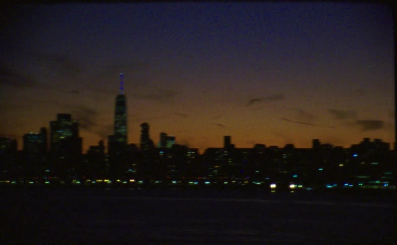 Vintage film footage captures abstract light streaks from a moving vehicle that resolves into a classic view of the New York City skyline at dusk