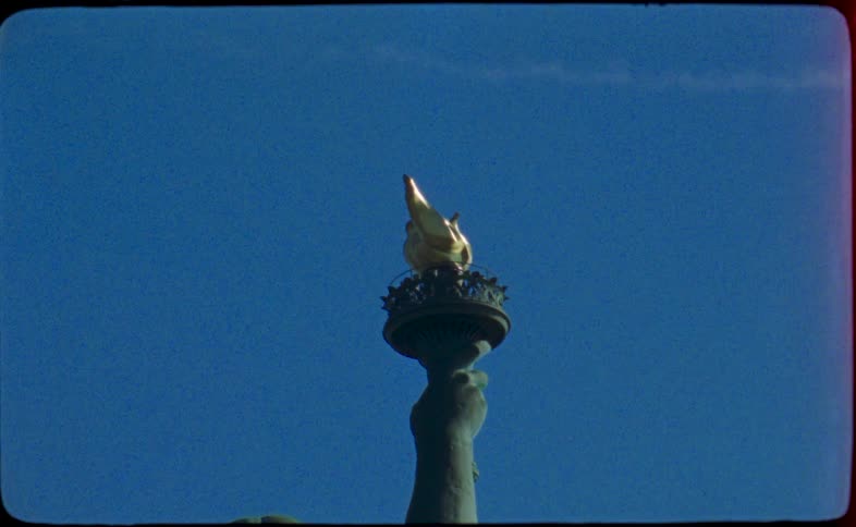An archival, low-angle shot captures the golden torch of the Statue of Liberty against a brilliant blue sky