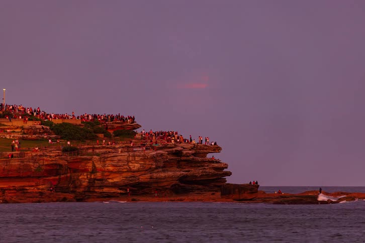 A beautiful timelapse shows crowds gathering on a rocky coastline to witness the spectacular rise of a blood moon lunar eclipse over the ocean