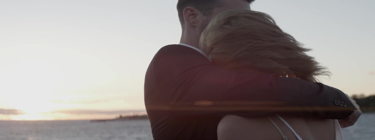A man and woman hug on a windy beach at sunset