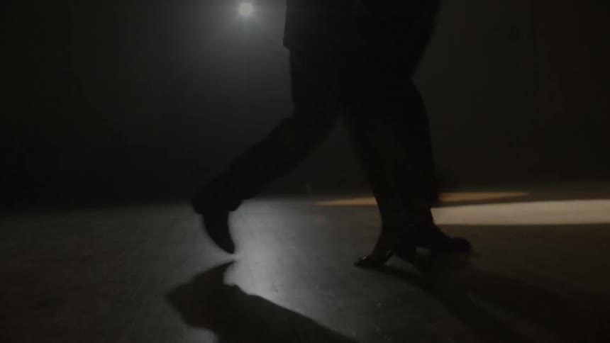 Two people dance together under a spot light