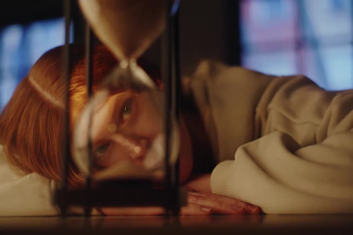 A melancholic red-haired woman watches time slip away through an hourglass, with the focus shifting from the falling sand to her pensive face