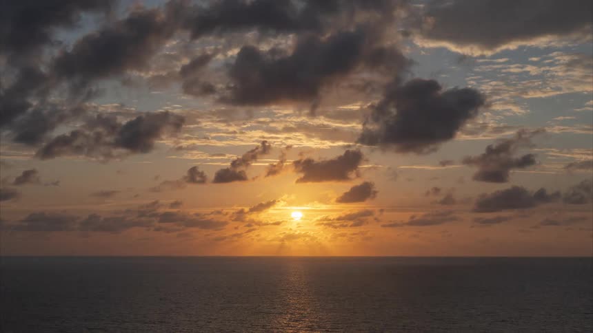 A breathtaking time-lapse captures the sun rising through dramatic clouds over the ocean horizon