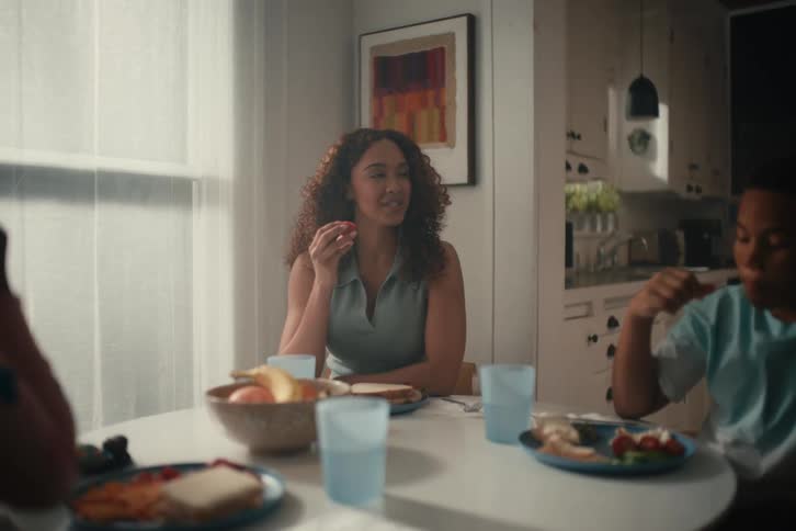 A cheerful mother and her two children playfully toast with strawberries while sharing a happy family meal at the dining table