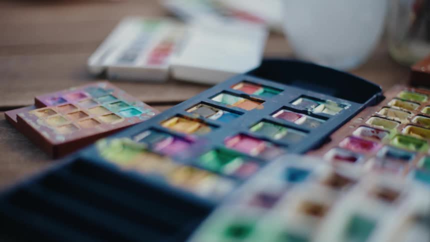 An artistic close-up of several watercolor paint palettes laid out on a rustic wooden table