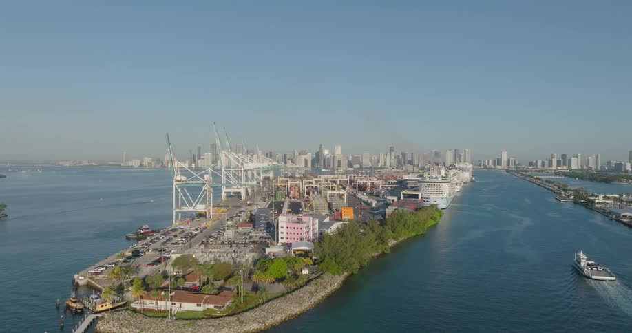 A rising aerial shot reveals the bustling Port of Miami, featuring massive container cranes and docked cruise ships set against the downtown skyline