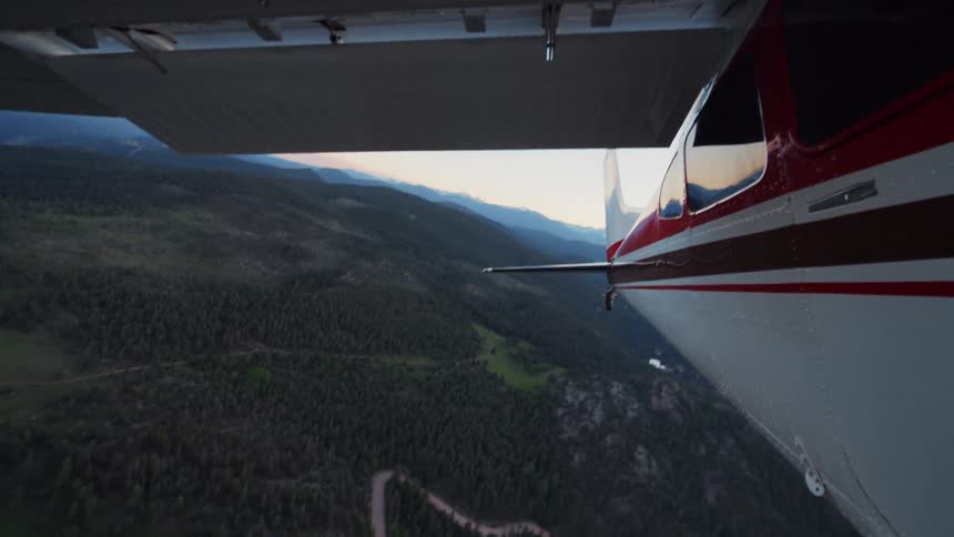 A serene aerial view from a small plane flying over a lush, forested mountain valley during a beautiful sunset