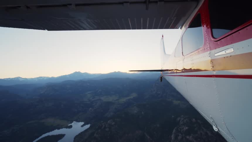 A serene aerial view from a small plane flying over a forest, mountains, and a lake at sunrise