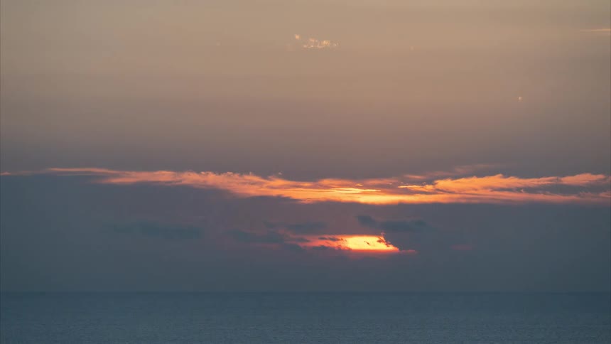A glorious time-lapse captures the golden sun rising from behind the clouds over the ocean