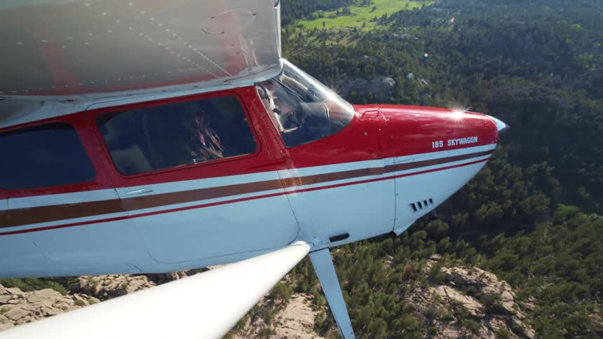 An aerial view from the wing of a small 185 Skywagon airplane as a pilot flies over a scenic mountain range
