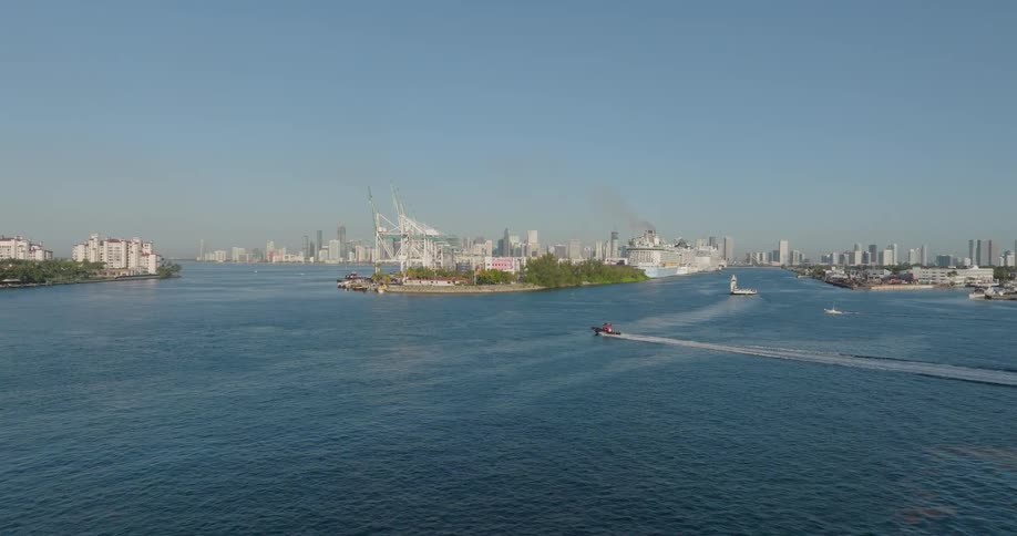 A scenic wide shot of the Port of Miami and the city skyline as a small boat cruises through the main channel on a sunny day