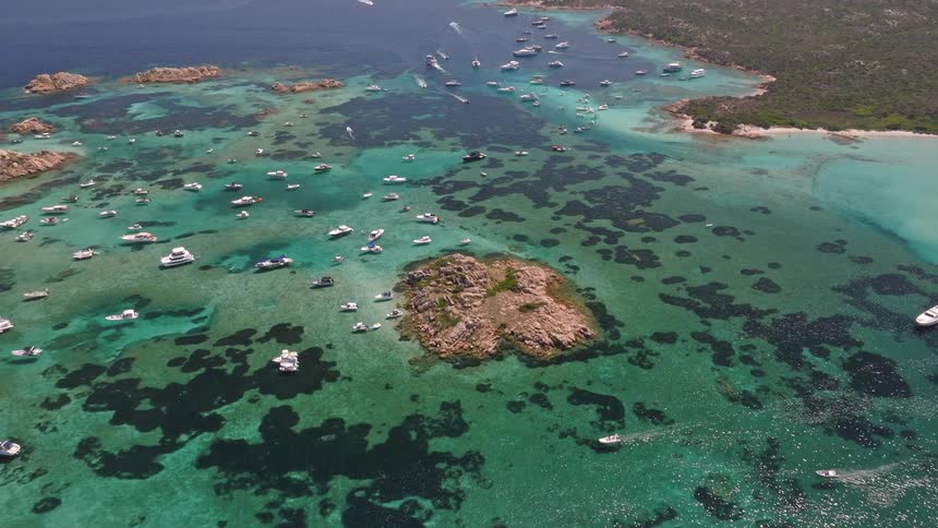 Stunning aerial view flying over a crowded bay filled with yachts and boats anchored in crystal clear turquoise water among rocky islands