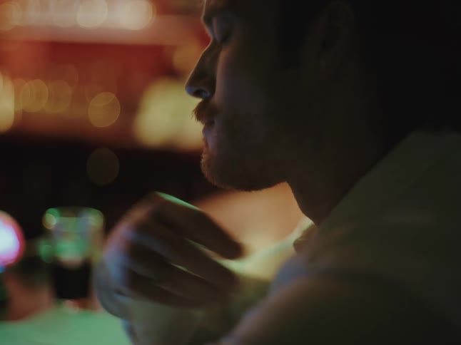 A moody close-up of a young man sitting alone in a dimly lit pub, appearing stressed and deep in thought