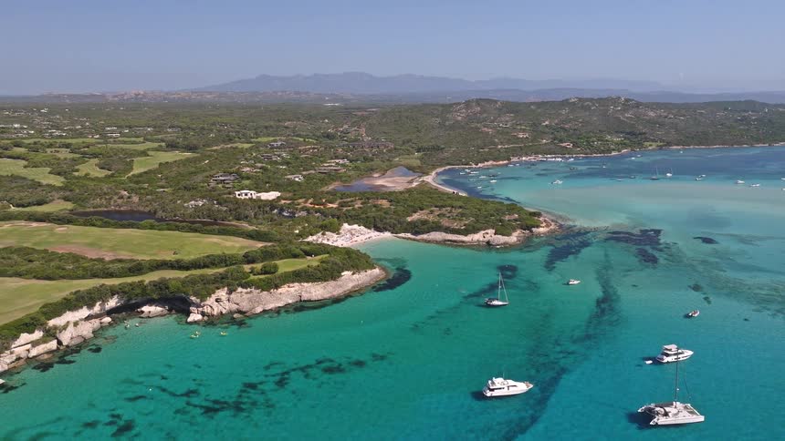 An aerial pullback shot reveals a breathtaking turquoise lagoon filled with anchored yachts and sailboats, surrounded by a lush green island coastline