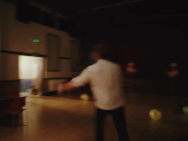 Motion-blurred shot of a man in a white shirt and tie dancing erratically and emotionally in a dimly lit, empty hall after a party