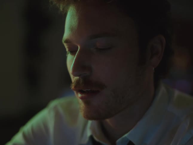 A handsome man with a mustache enjoys a moment of pleasure, smiling contentedly with his eyes closed in moody lighting
