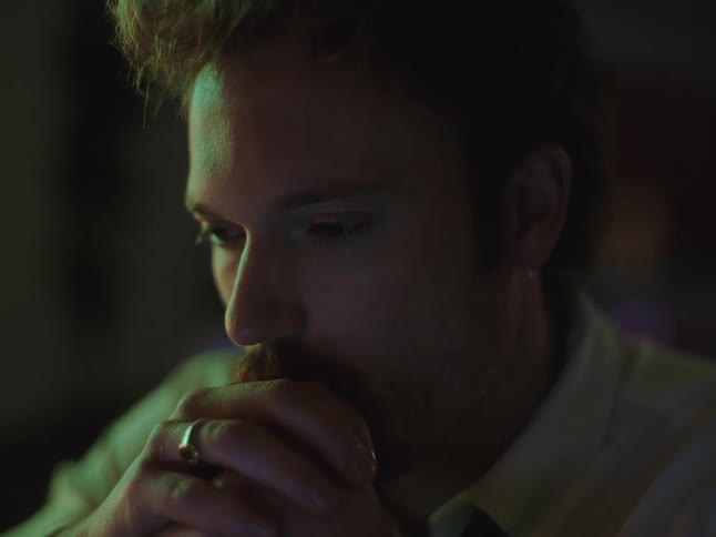 Close-up of a tired and stressed young man with a mustache rubbing his face and temples in a dark, moody room