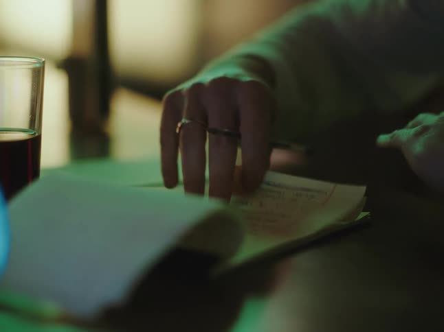 Close up of a person's hands writing notes in a notepad with a pen under moody green light