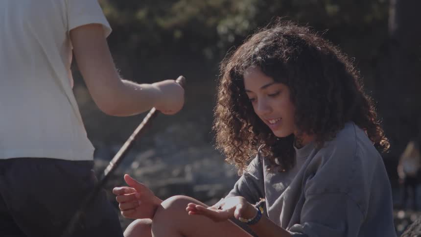 A curious teenage girl examines a small creature her friend found while they explore the outdoors together