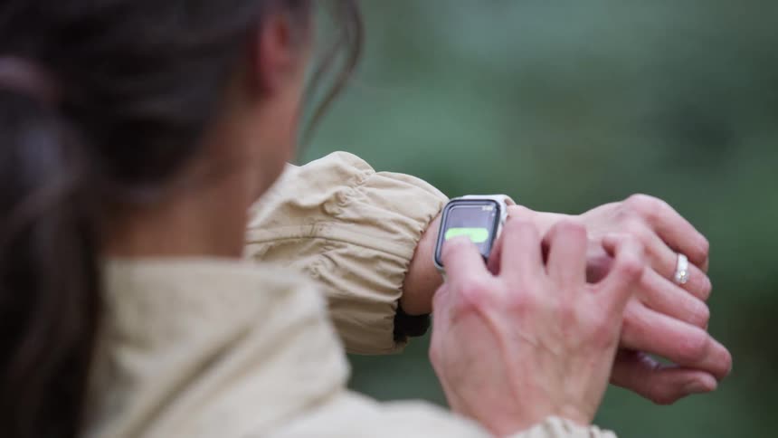 A woman checks her fitness progress on her smartwatch while on an afternoon walk outdoors