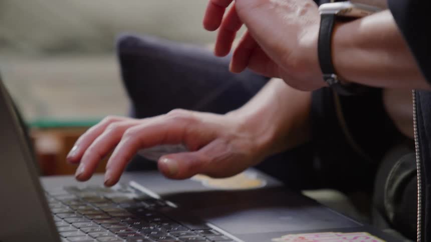 A close-up slow motion shot of a woman's hands typing on a laptop before checking her smartwatch and closing it