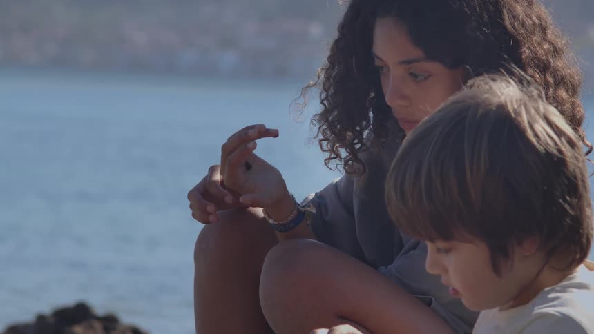 A caring older sister shows her curious younger brother a small sea creature she found while sitting on the sunny beach