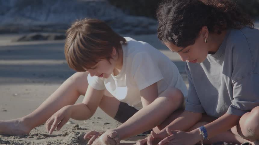Two friends, a boy and a girl, sit together on the sandy beach playing and building a sandcastle