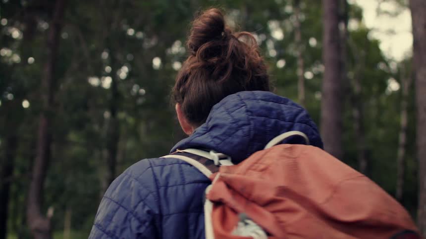 Close up of a male hiker turning to walk towards a beautiful, expansive view of a green valley