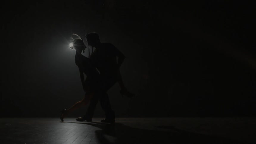 Two dancers hold each other in a dark room