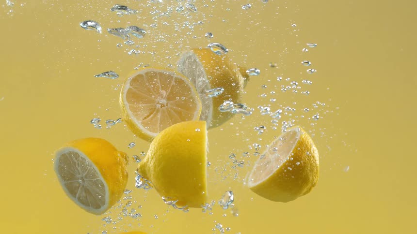 Cinemagraph of fresh sliced lemons floating in sparkling water with bubbles against a vibrant yellow backdrop