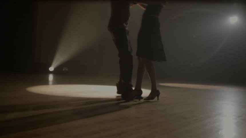 The legs of a man and woman intertwine as they dance on a wood floor
