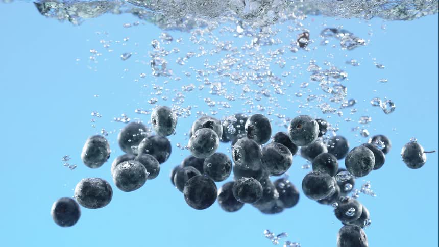 A handful of fresh blueberries plunges into clear water, creating a cascade of bubbles in super slow motion