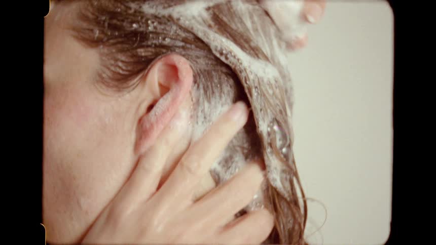 A vintage home video style close-up of a woman lathering her hair with shampoo