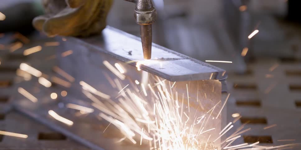 A worker is cutting a metal beam with a torch