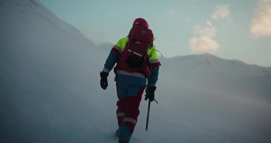 A lone mountaineer with a backpack and ice axe makes a slow and steady ascent up a challenging, snow-covered mountain